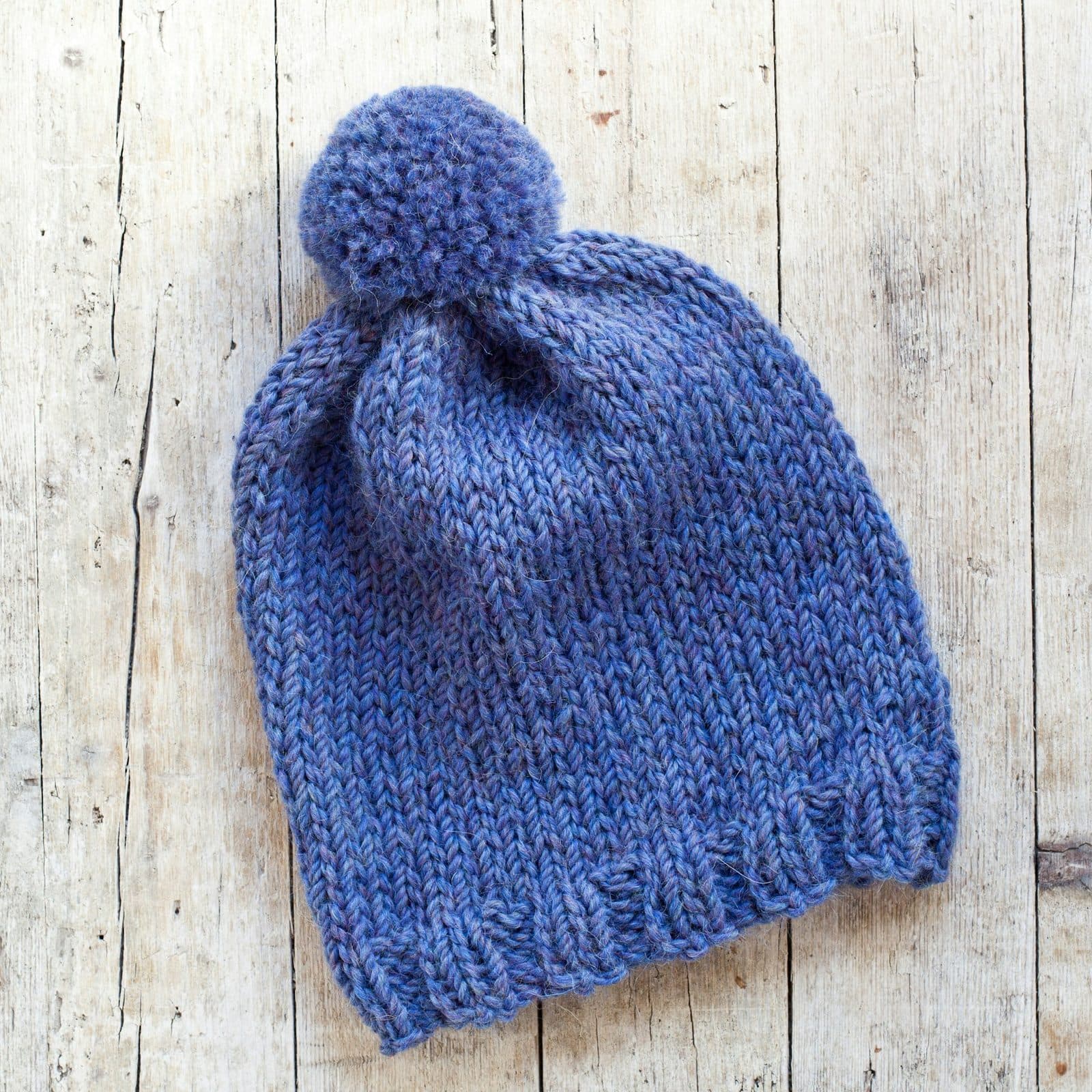 Gorro de punto azul con pompón sobre madera clara