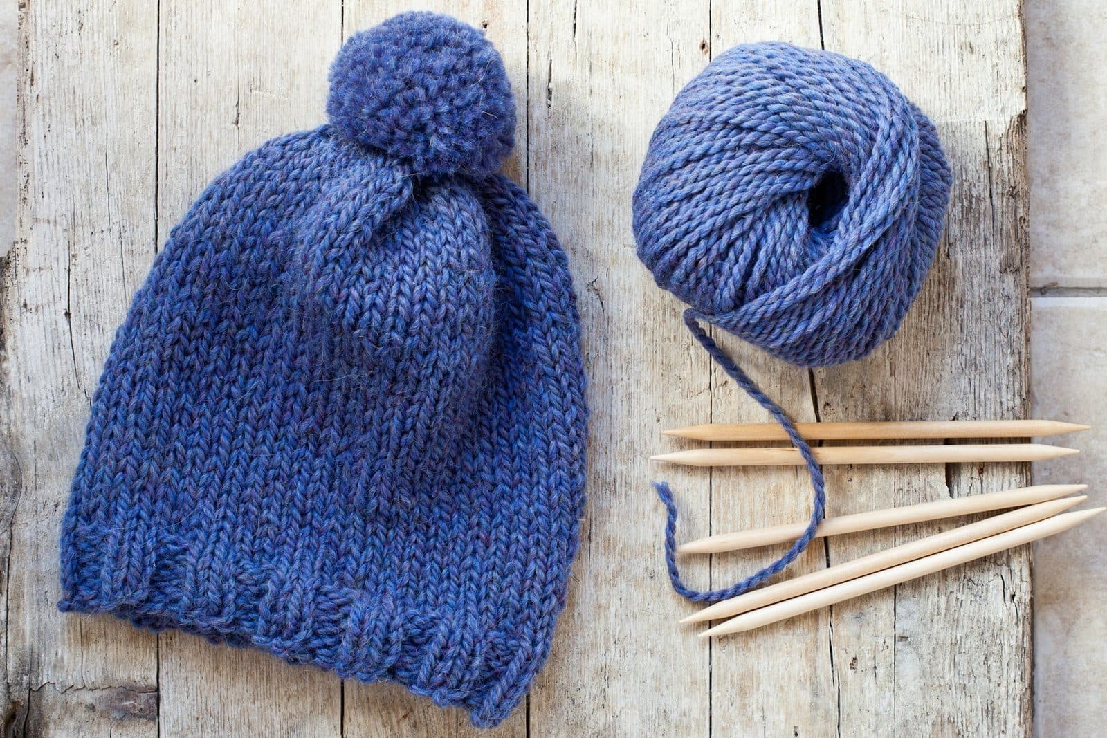 Gorro de punto azul con pompón, ovillo a juego y agujas de madera