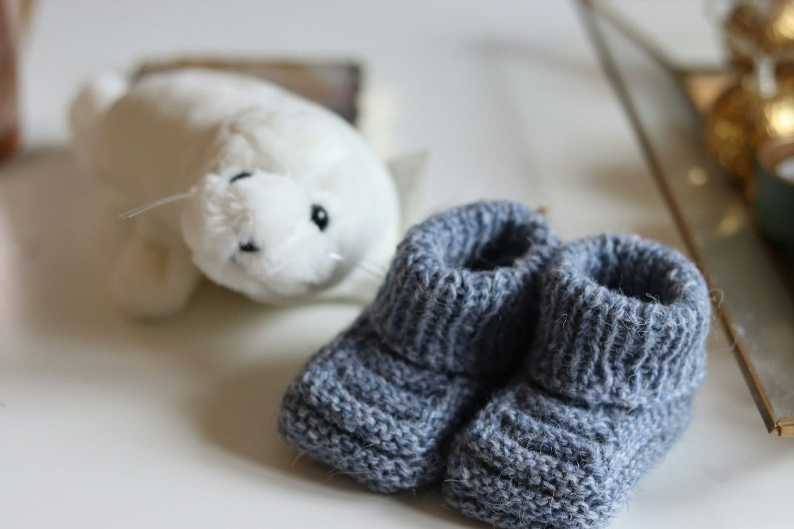 Patucos de punto gris azulado junto a una foca de peluche blanca